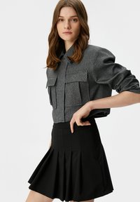 Graues, strukturiertes Hemd mit zwei Fronttaschen, kombiniert mit einem schwarzen, plissierten Rock. Verfügt über ein Knopfdesign und eine taillierte Passform.