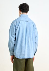 Lichtblauwe spijkerblouse met een klassieke kraag, knoopmanchetten en een relaxed fit. De achterkant heeft een centrale plooi en een afgeronde zoom.