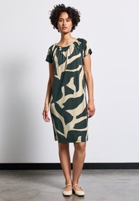 Kortärmad klänning med samlad halsringning, prydd med ett grönt och beige abstrakt mönster på mjukt tyg. Knälång klipp med rak fåll.