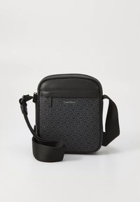 Bolso bandolera Calvin Klein en tela negra con un sutil patrón de logo, que cuenta con un bolsillo frontal con cremallera y una correa ajustable.