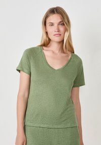 T-shirt vert en V, fabriqué en tissu doux et texturé, avec des manches courtes et une coupe décontractée, présentant un ourlet légèrement plus long pour plus de confort.