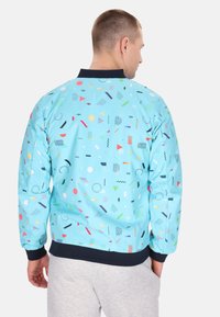 Lichtblauwe bomberjack met een geometrisch patroon van kleurrijke vormen. Contrasterende marineblauwe kraag en manchetten, zachte textuur, pullover stijl.