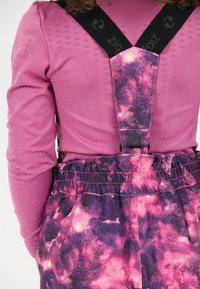Pink long-sleeve top with textured fabric paired with purple and pink galaxy-patterned overalls featuring black adjustable straps.