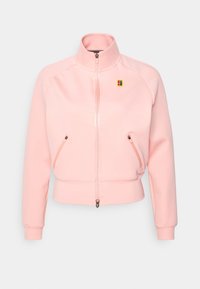 Chaqueta rosa de cremallera hecha de tela suave con puños y dobladillo acanalados. Presenta dos bolsillos frontales con cremallera y un pequeño logo en el pecho.