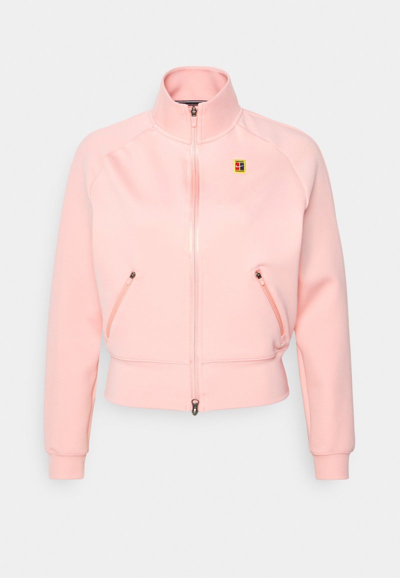 Chaqueta rosa de cremallera hecha de tela suave con puños y dobladillo acanalados. Presenta dos bolsillos frontales con cremallera y un pequeño logo en el pecho.