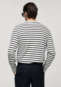 Langärmliges gestreiftes Hemd in Weiß und Marineblau mit Rundhalsausschnitt und lockerem Schnitt, kombiniert mit dunklen Hosen. Sichtbares Detail des strukturierten Stoffes.