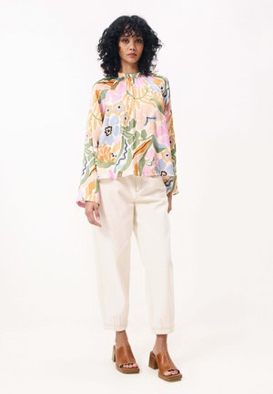 Bluse mit floralem Druck und langen Ärmeln, gerafftem Ausschnitt, kombiniert mit hellbeigen Hosen und braunen Sandalen mit Absatz.