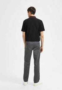 Črna polo majica z rdečimi dodatki, sivi hlače in bele superge. Outfita je sproščena in prikazuje sodobno prileganje ter teksturo materiala.