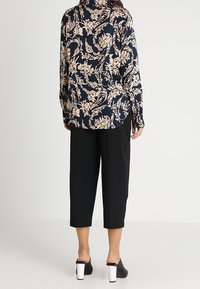 Tmavě modrá halenka s dlouhými rukávy a krémovým květinovým vzorem, spárovaná s černými zkrácenými kalhotami a černými mules s bílými blokovými podpatky.