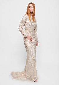 Langärmliges Kleid in hellem Beige mit aufwendiger Perlenstickerei und Pailletten, das eine figurbetonte Silhouette und einen fließenden Schleppe bietet.