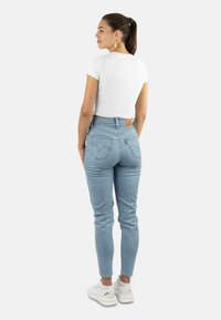 Helle blaue, hochgeschnittene Jeans mit leichtem Stretch, ausgestattet mit einem braunen Lederetikett auf der Rückseite, kombiniert mit einem taillierten weißen Kurzarmoberteil.