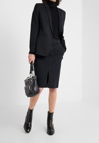 Blazer noir, col roulé noir, jupe crayon en denim noir avec fente avant, bottines noires, et un petit sac à main clouté noir.