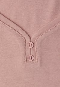 Jasnoróżowa, teksturowana tkanina z dekoltem w serek. Dwa okrągłe, jasno różowe guziki podkreślają plisę. Czyste szwy i dopasowany krój.