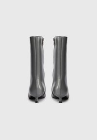 Pelēki āda vidēja garuma zābaki ar aizmugures rāvējslēdzējiem un zemu smailu papēdi uz balta fona, skatoties no aizmugures.