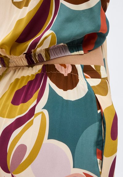 Κοντινό πλάνο πολύχρωμου αφηρημένου σχεδίου σε ελαστική μέση ρούχου με αποχρώσεις τιρκουάζ, μουσταρδί, καφέ, μωβ και κρεμ.