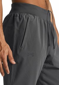 Graue Sporthosen aus leichtem Material, mit einem elastischen Bund und einer Zugkordel, seitlichen Taschen und einem dezenten Logo.