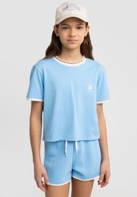 Jasnoniebieski crop top z białym wykończeniem, zdobiony niewielką grafiką kwiatową; pasujące jasnoniebieskie szorty z białymi lamówkami i sznurkiem.