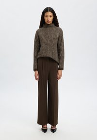 Rudas zigzag raštas megztinis su aukštu kaklu ir ilgomis rankovėmis, derinamas su aukštu juosmeniu rudiems plačiakojams kelniams ir juodais smailiais aukštakulniais.