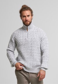 Grijze gebreide trui met een gestructureerd kabelpatroon, een hoge kraag en een halve rits met een houten accent. Zacht, warm materiaal.