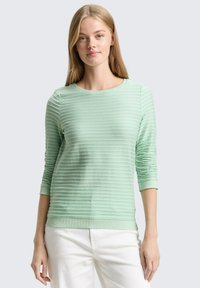 Lichtgroene textuursweater met horizontale strepen, ronde hals en lange mouwen, gecombineerd met witte broek. Zacht gebreid materiaal.