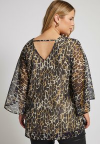 Top in stampa animale trasparente con schiena a forma di V, maniche libere e una combinazione di marroni, neri e viola nel motivo leopardato.