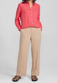 Korallfärgad linneknappskjorta som matchas med ljusbeiga högmidjade vida byxor. Sandalerna har en neutral rem och enkel hårdvara.