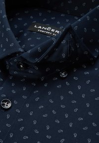 Granatowa koszula wykonana z gładkiego materiału, zdobiona białym wzorem paisley, z klasycznym kołnierzykiem i dwoma czarnymi guzikami z przodu.