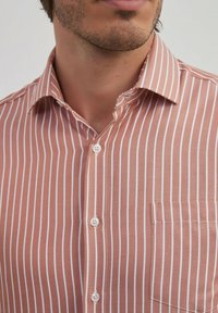 Chemise à rayures en tissu rose clair avec des rayures verticales blanches, col à revers et poche poitrine avec fermeture à bouton.