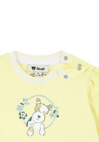 Camicia di cotone gialla con maniche corte, caratterizzata da un'illustrazione di un cane circondato da fiori. Collo leggermente elastico con bottoni a pressione.
