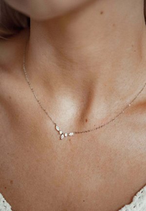 Delicado collar de cadena de plata con cinco pequeñas gemas claras de formas diferentes que descansan en la base del cuello de una persona.