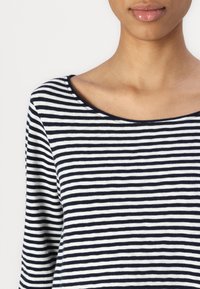 Stripet langermet topp i marineblått og hvitt. Myk stoff, bred scoop-hals, og fine horisontale striper. Uformell design, lett tekstur.