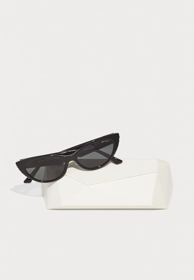 Black cat-eye sunglasses with gradient lenses, resting on a white geometric case. Sunglasses feature slim arms and a glossy finish.