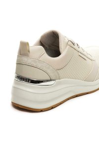 Sneaker beige con superiore testurizzato, pannelli perforati e accento cromo sul tallone. Presenta una suola bianca spessa e una suola in gomma.