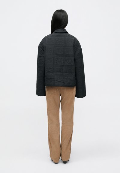 Must mustriga jakker, millel on geomeetrilised mustrid, laiad varrukad ja krae, koos heledate pruunide corduroy pükstega.