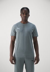Grå kortermet treningsskjorte i et glatt stoff med en hvit Puma-logo på venstre bryst; kombinert med matchende grå bukser.