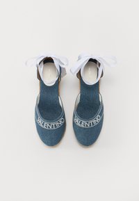 Denimové espadrilky s kulatou špičkou, bílým páskem se značkou a bílými stuhovými tkaničkami. Podešev je vyrobena z hnědého jutového materiálu.