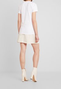 Vit bomulls t-shirt med kort ärm, i kombination med en ljusbeige kjol med sömnadsdetalj. Glansiga beige ankelstövlar med klack.