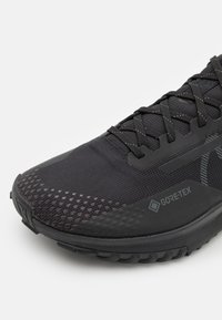 Chaussure de running noire avec une tige en mesh, présentant un embout texturé, une marque GORE-TEX et une semelle extérieure avec motif de grip.