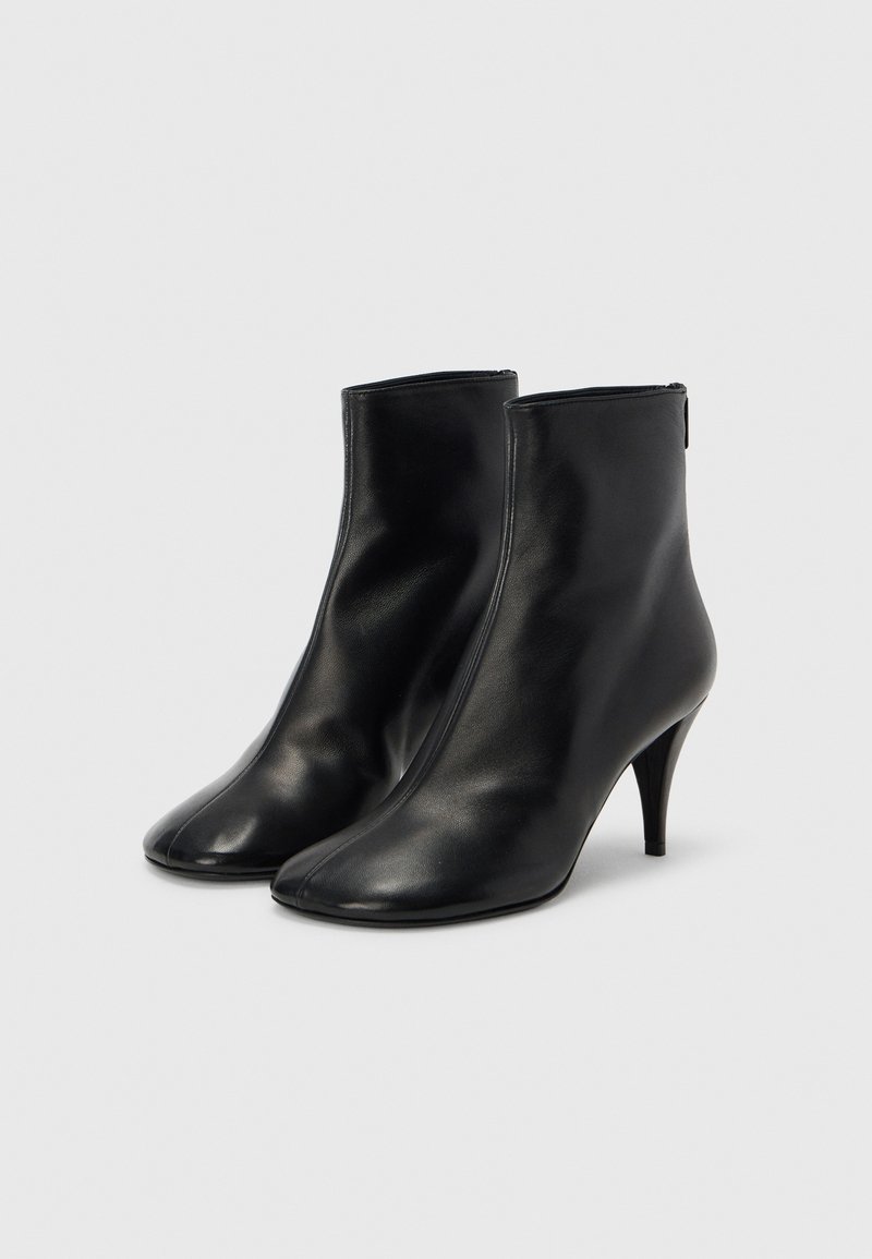 Bottes cuir noires pour cheville avec bout pointu, talon fin et design minimaliste. Texture lisse avec fermeture éclair à l'arrière.