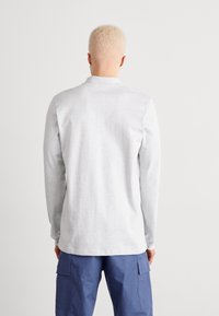 Långärmad grå polo med mjuk textur, vikbar krage och rak nederkant, som bärs med blåa cargobyxor.