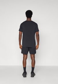 Black athletic t-shirt with short sleeves, paired with black shorts. The fabric appears lightweight and smooth, offering a relaxed fit.