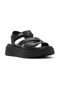 Sandali con piattaforma nera in pelle, con cinturini incrociati e un accent decorativo dorato. La suola nera spessa e testurizzata offre stabilità.