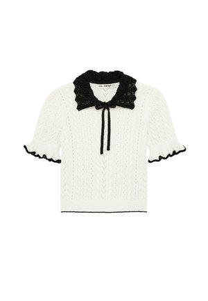 Maglione bianco a maniche corte in maglia con colletto in pizzo smerlato nero, fiocco nero al collo e bordi neri sulle maniche arricciate e sull'orlo.