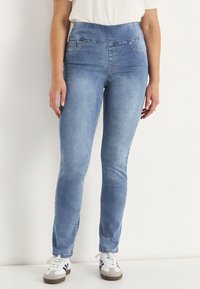 Blå slim jeans i denim med hög midja, med framfickor och lätt tvätt över låren, bärs med vita sneakers.