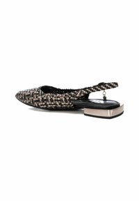 Zapato plano tejido en negro y beige, con punta afilada, tira trasera y un bajo tacón cuadrado metálico. Tela texturizada con un patrón intrincado.