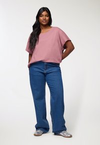Kostkowa różowa bawełniana koszulka z okrągłym dekoltem, w połączeniu z szerokimi niebieskimi dżinsami oraz srebrnymi sneakersami. Gładka tekstura i swobodny krój.