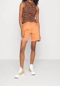 Brun ärmlös topp med en strukturerad, rynkad design, parat med orange denimshorts med fransade kanter och beige hög-top sneakers.