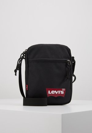 Sac bandoulière en tissu noir avec fermeture éclair, sangle réglable et logo Levi's rouge. Doté d'une poche avant et d'une surface texturée.