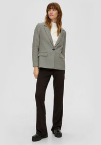 Maßgeschneiderter Hahnentritt-Blazer in Schwarz und Weiß, mit einem einzigen Knopfverschluss, Reverskragen und zwei vorderen Taschen, kombiniert mit schwarzen Hosen.