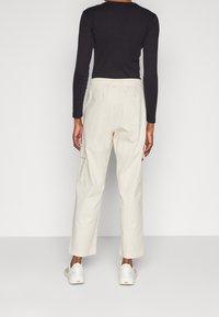 Bílé cargo kalhoty s uvolněným střihem a elastickým pasem, obsahující dvě boční kapsy. V kombinaci s bílými teniskami a černým topem s dlouhým rukávem.